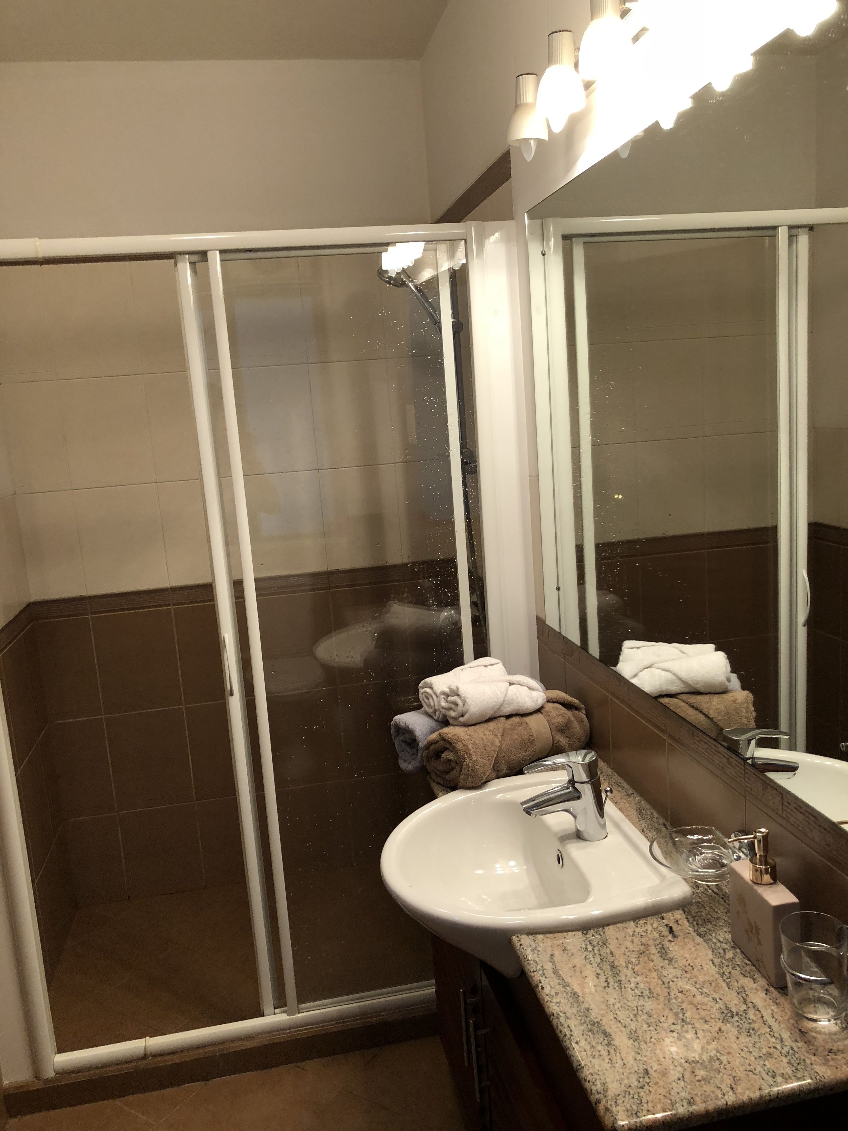 A bathroom with a glass-enclosed shower, a sink with a granite countertop, and a mirror above the sink.