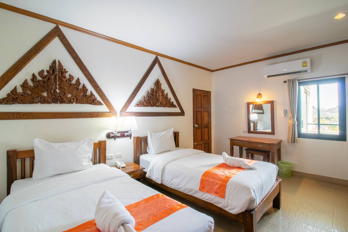 A hotel room with two beds, wooden headboards, a desk, a mirror, and a window with a view.