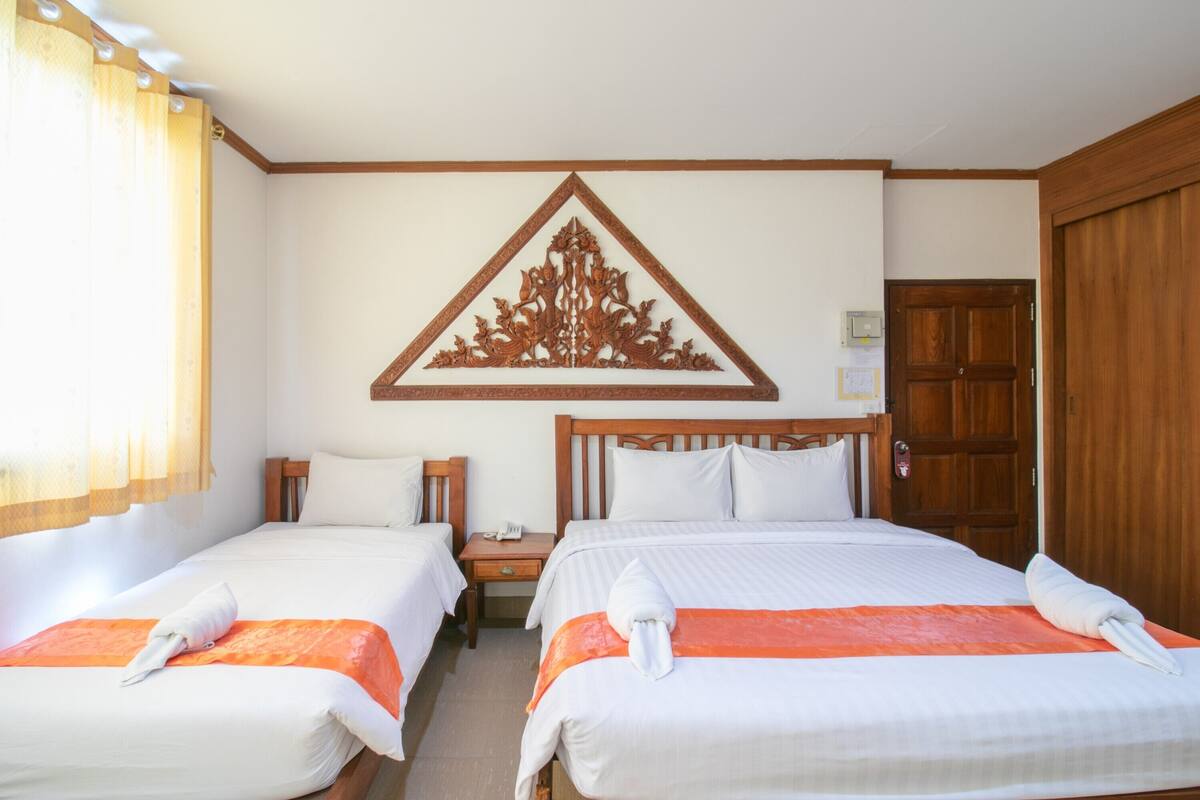 A hotel room with two beds, a wooden headboard, a wall-mounted decorative piece, and a wooden door.