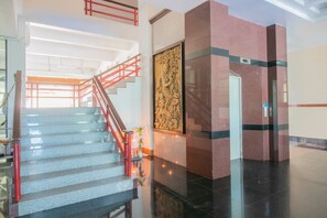 A modern hotel lobby with a marble staircase, a decorative wall sculpture, and a red railing. - Onnicha Hotel (Ratsada)