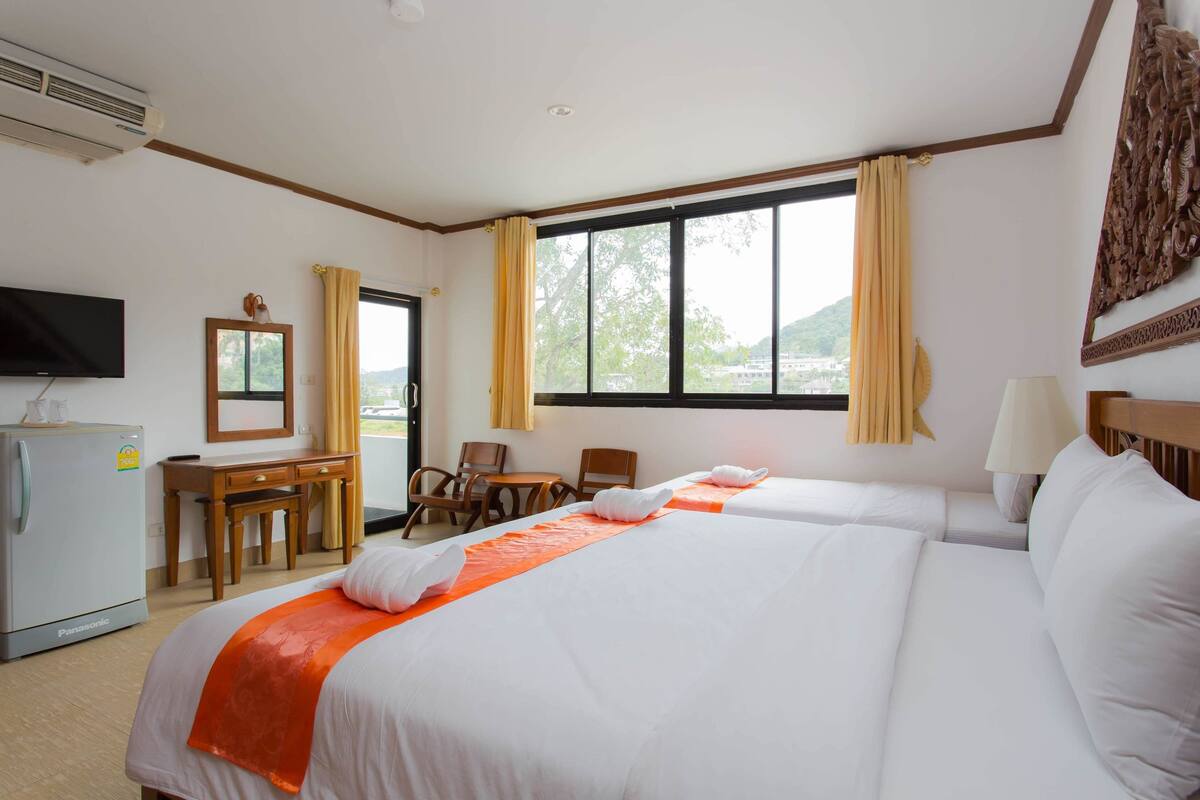 A hotel room with two beds, a desk, a chair, a television, and a refrigerator.