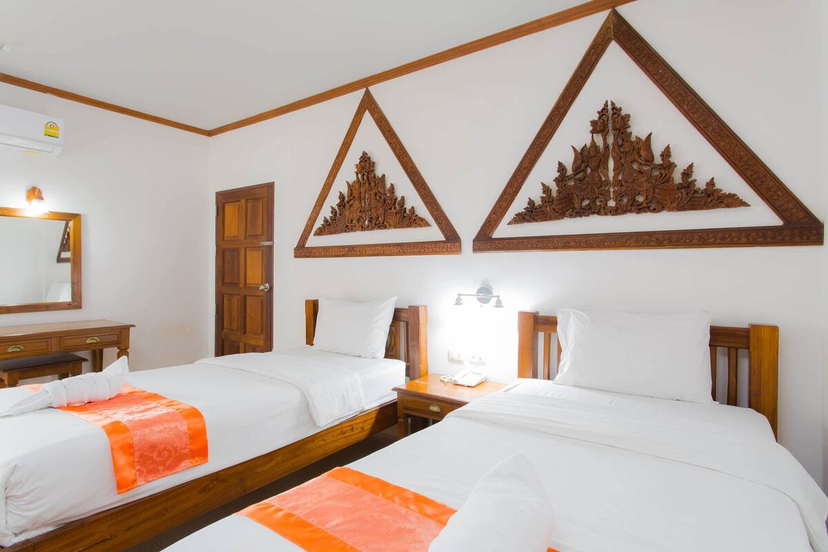 A hotel room with two beds, wooden headboards, a wooden dresser, a mirror, and wall-mounted artwork.