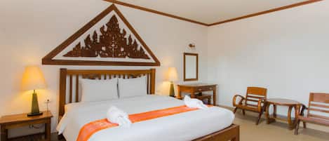 Una habitación de hotel con una cama grande, dos mesitas de noche con lámparas, una silla de madera y una pequeña mesa.