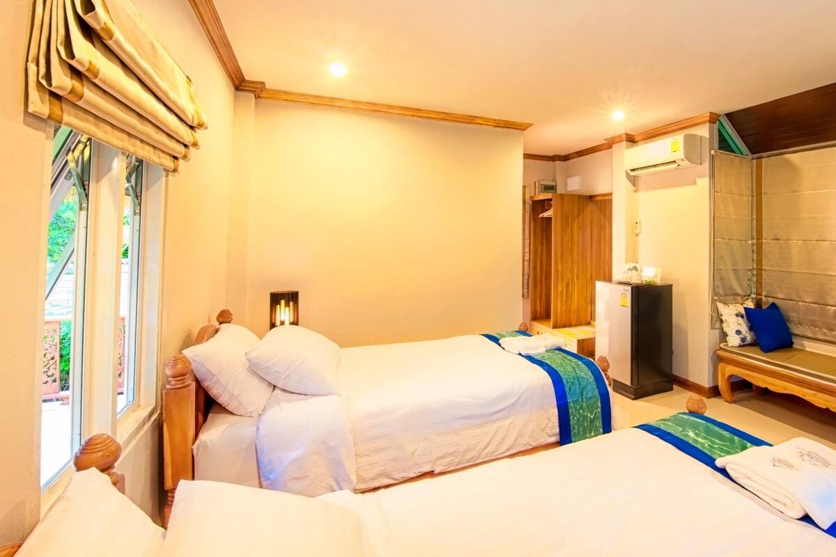 A hotel room with two beds, a bench, a mirror, and an air conditioning unit.