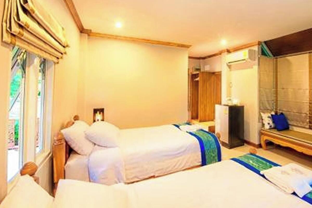 A hotel room with two beds, a large mirror, a bench, and a view of the outdoors.