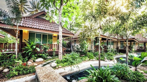 Un edificio de estilo tradicional con tejado de baldosas, rodeado de exuberante vegetación y un pequeño estanque.