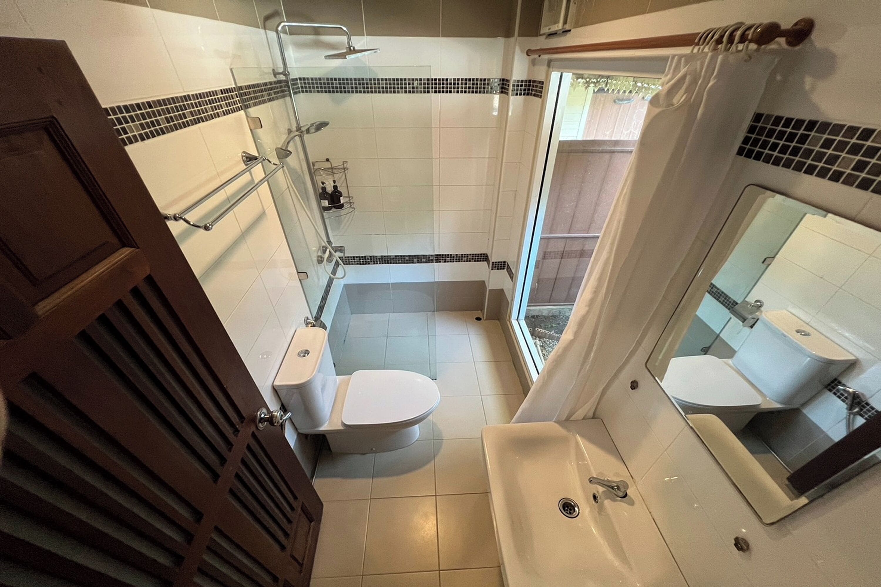 Un baño con ducha, dos inodoros, un lavabo y un espejo.