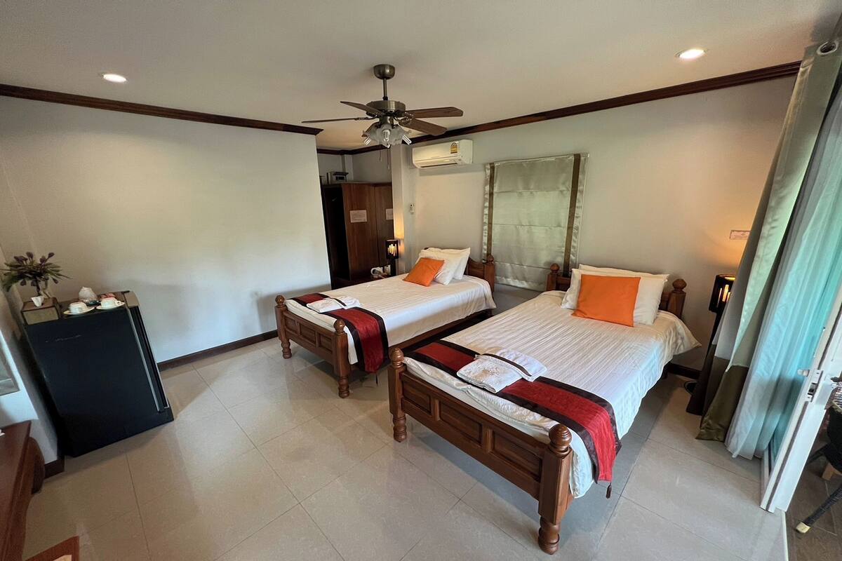 A hotel room with two wooden beds, a ceiling fan, an air conditioning unit, a small desk, and a cabinet.