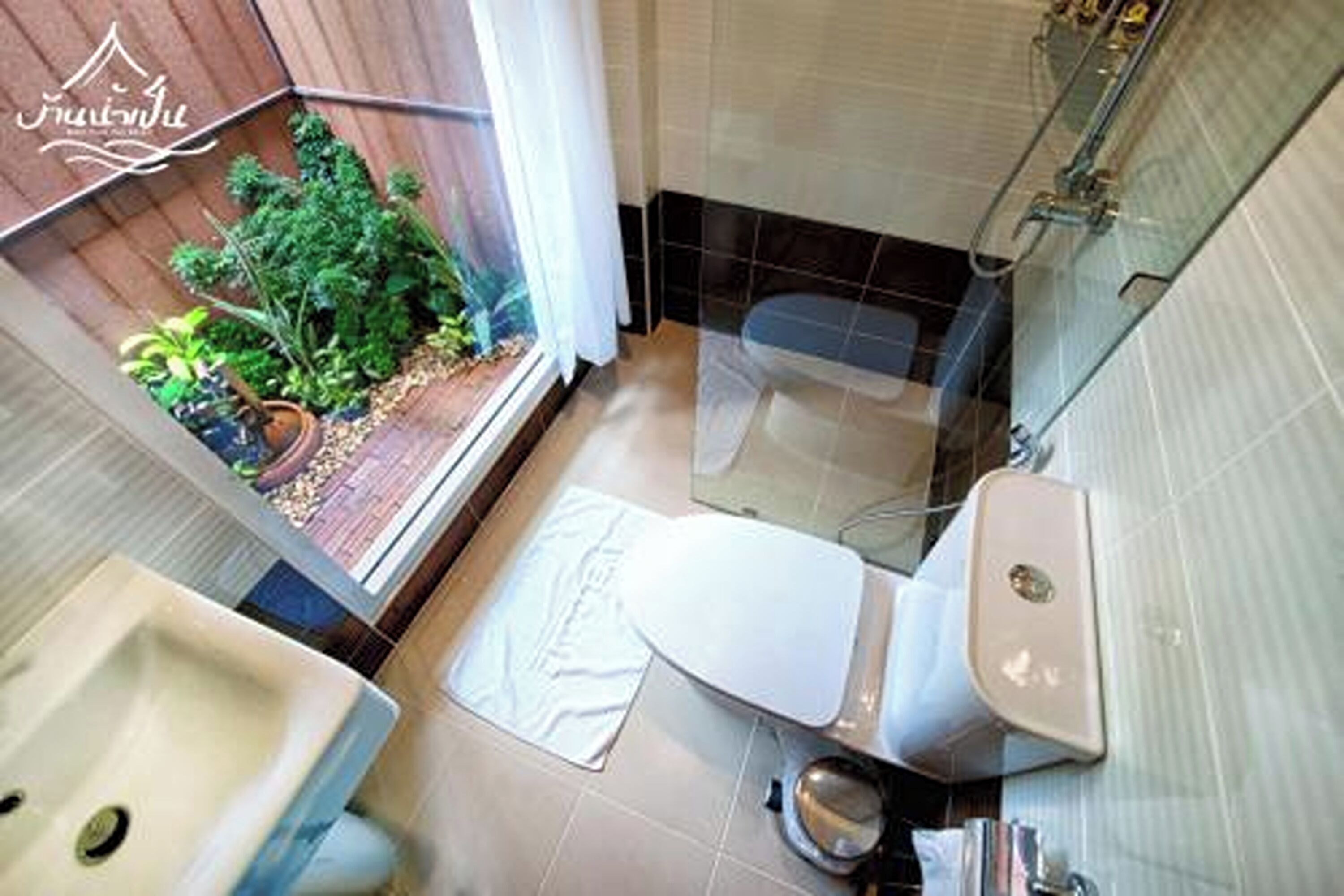 Et badeværelse med toilet, håndvask og bruseområde. Der kan anes en lille have gennem vinduet.