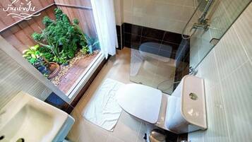 Et badeværelse med toilet, håndvask og bruseområde. Der kan anes en lille have gennem vinduet.