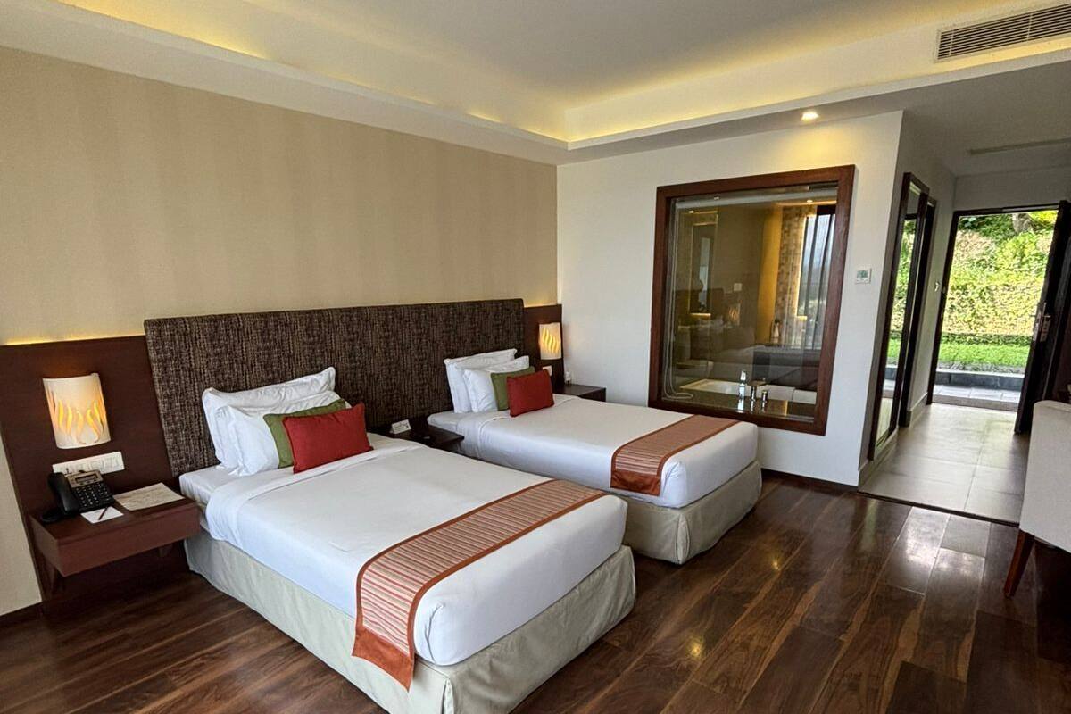 Habitación de hotel con dos camas, piso de madera, un espejo grande y vista al exterior.