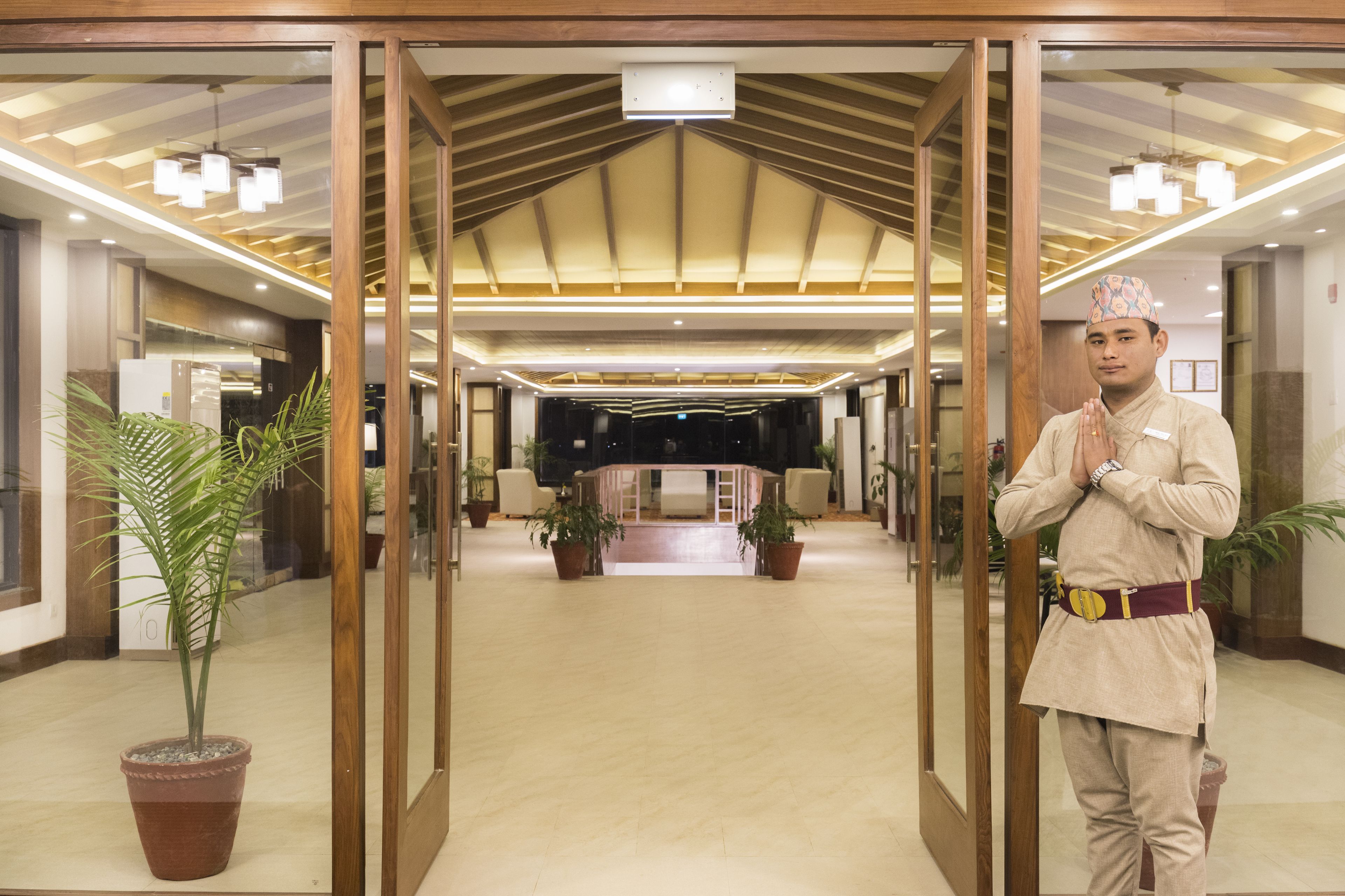 A hotel lobby with a modern design, featuring a central seating area, potted plants, and a person in traditional attire.