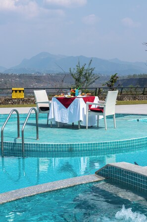 Une piscine avec une table et des chaises installées pour les repas, le tout entouré de montagnes.