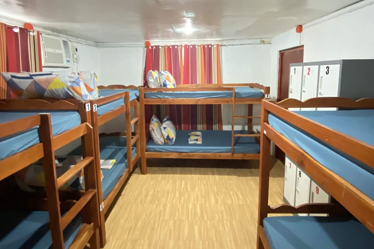 Een slaapzaal met stapelbedden, een houten vloer en een plafondventilator.