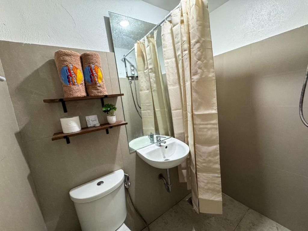Un baño con inodoro, lavamanos y cortina de ducha. Hay toallas y un estante pequeño con artículos de aseo.