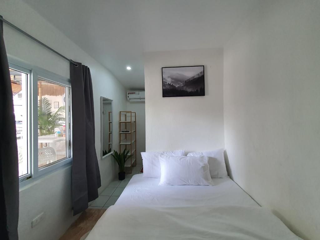 Un dormitorio con cama, una ventana con cortinas, un cuadro colgado en la pared y una planta pequeña.