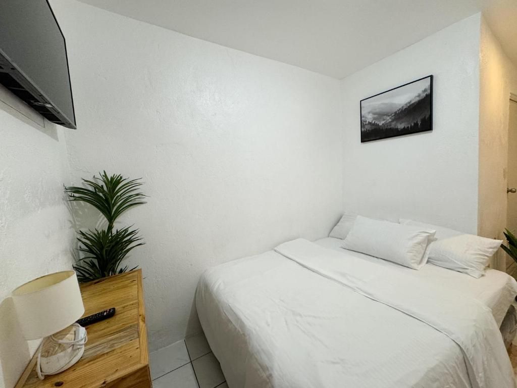 A bedroom with a bed, a TV mounted on the wall, a small table with a lamp, and a framed picture.