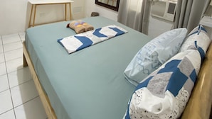 Une chambre à coucher avec un lit, un téléviseur fixé au mur, un petit bureau et une fenêtre avec des rideaux.