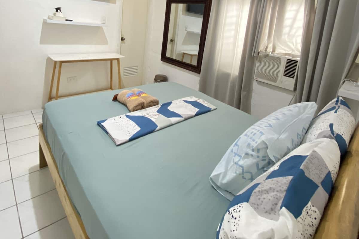 Een slaapkamer met een bed, een tv aan de muur, een klein bureau en een raam met gordijnen.