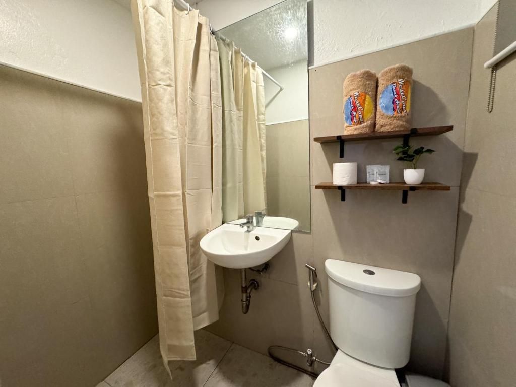 A bathroom with a shower curtain, a sink, a toilet, and shelves with towels and a plant.