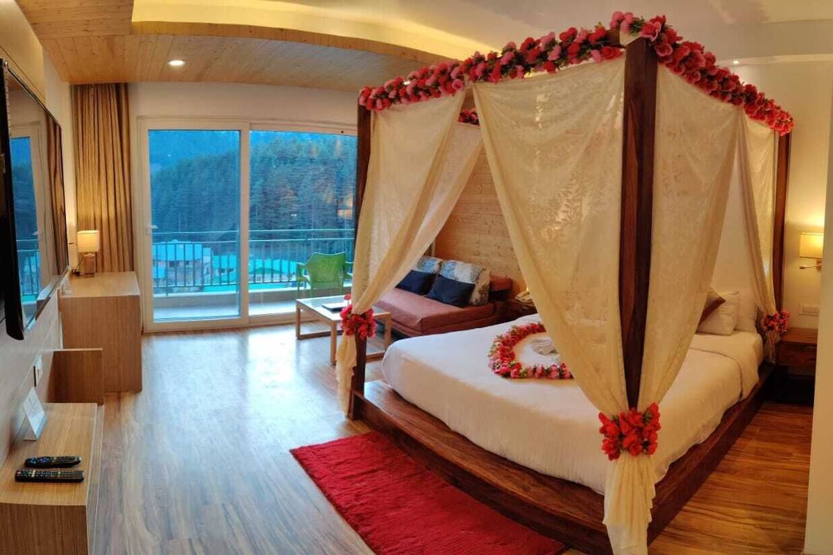 Una cama con dosel y dosel, un televisor, un escritorio con una silla y un balcón con vistas a árboles.