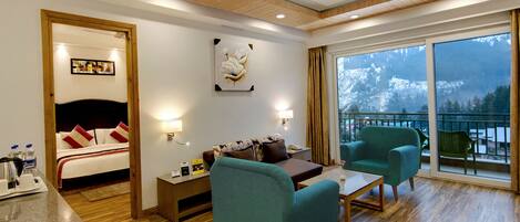 Een hotelkamer met een bed, een bank, een stoel, een tafel en een balkon met uitzicht op de bergen.