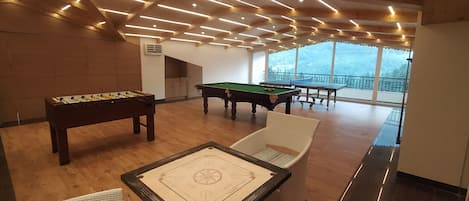 A billiards room with a pool table, a foosball table, and a foosball table with a star design.