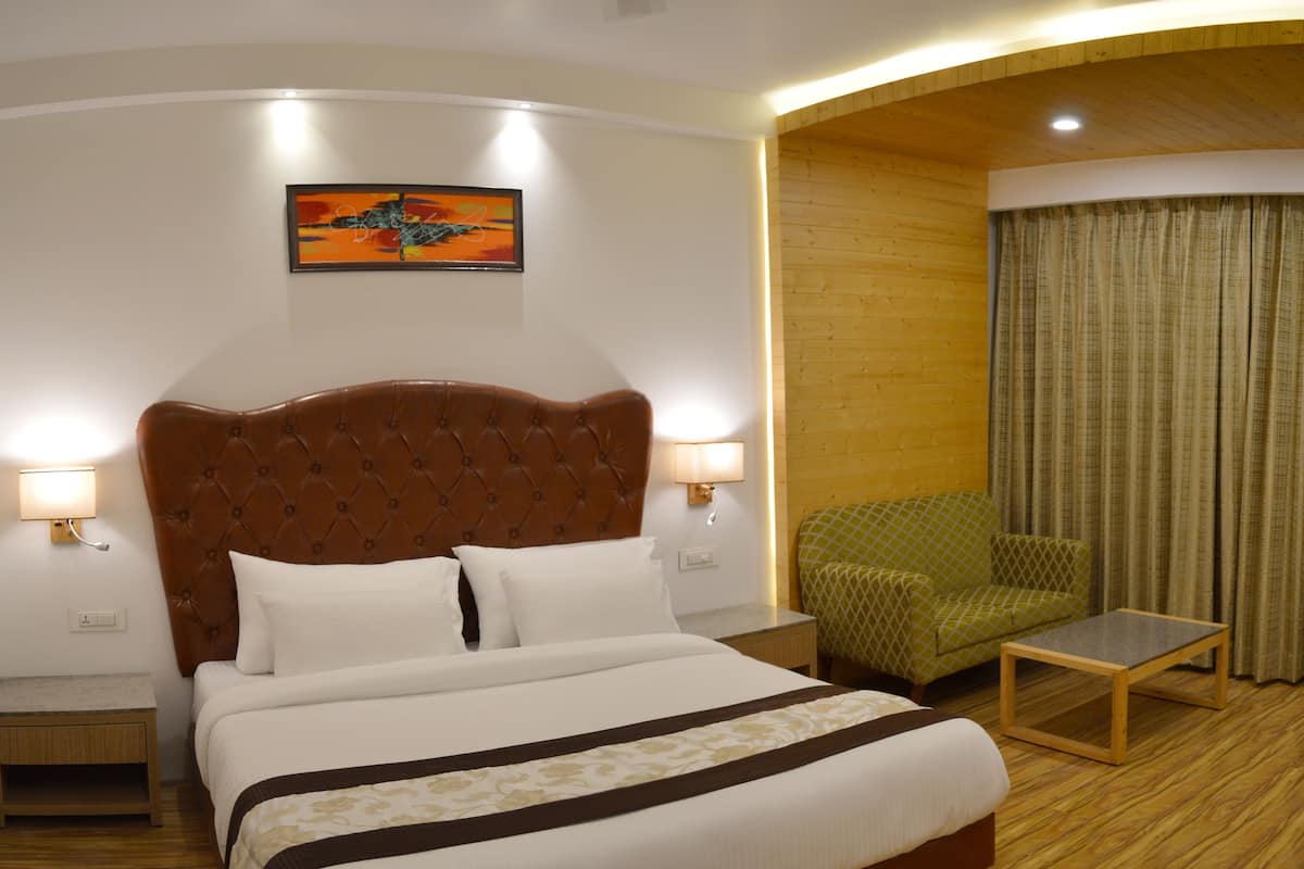 Una habitación de hotel con una cama grande, un sillón verde, una mesita y un cuadro en la pared.