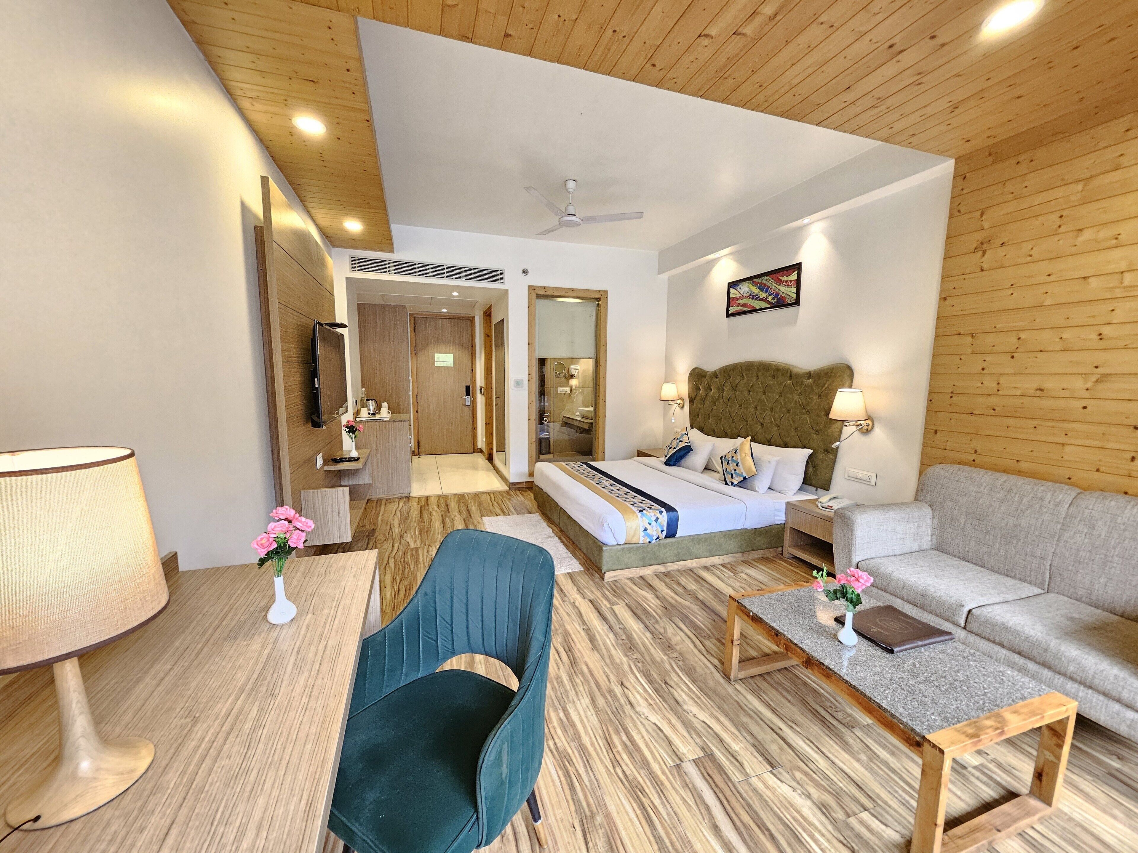 A hotel room with a bed, a sofa, a chair, a coffee table, and a desk with a lamp.