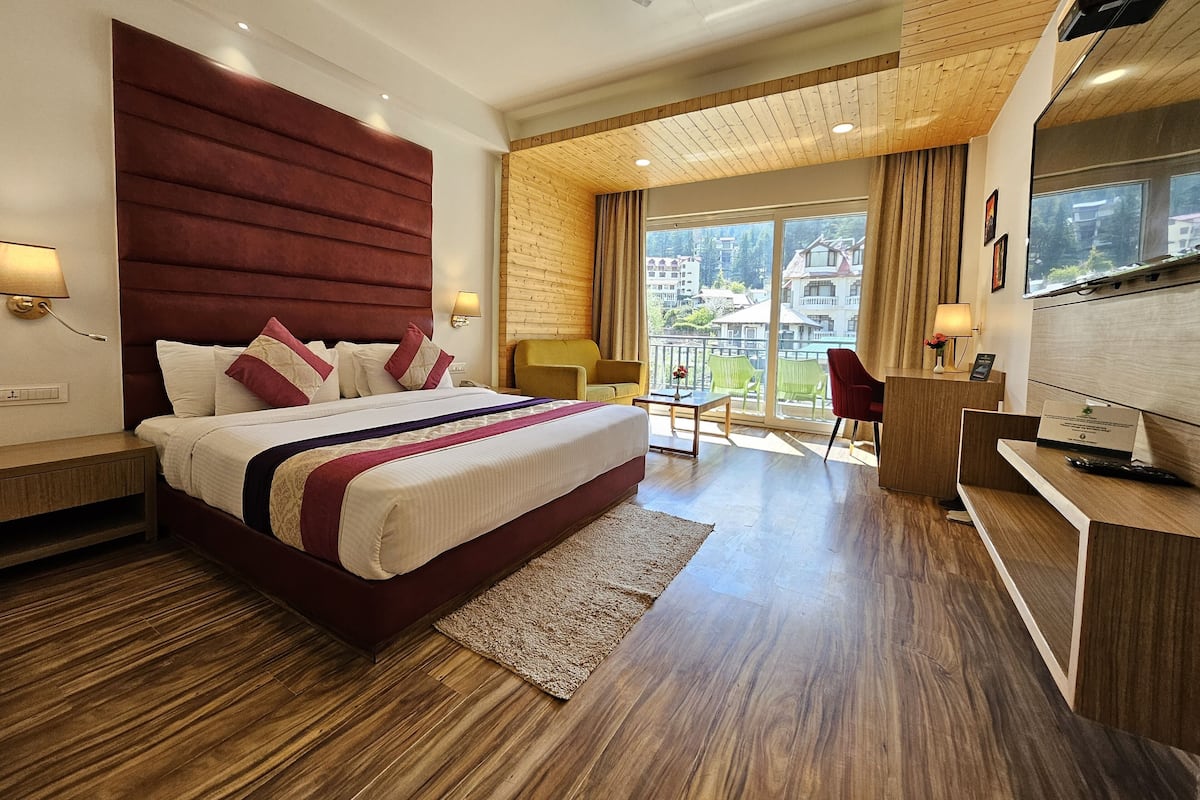 Una habitación de hotel moderna con una cama grande, suelo de madera, un escritorio y un balcón con vistas a edificios.