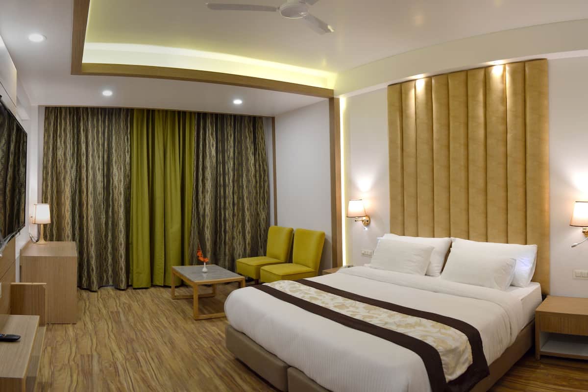 Habitación de hotel con cama, escritorio, silla, televisión y ventana con cortinas.