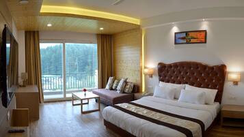 A hotel room with a large bed, a sofa, a TV, and a balcony with a view of trees.