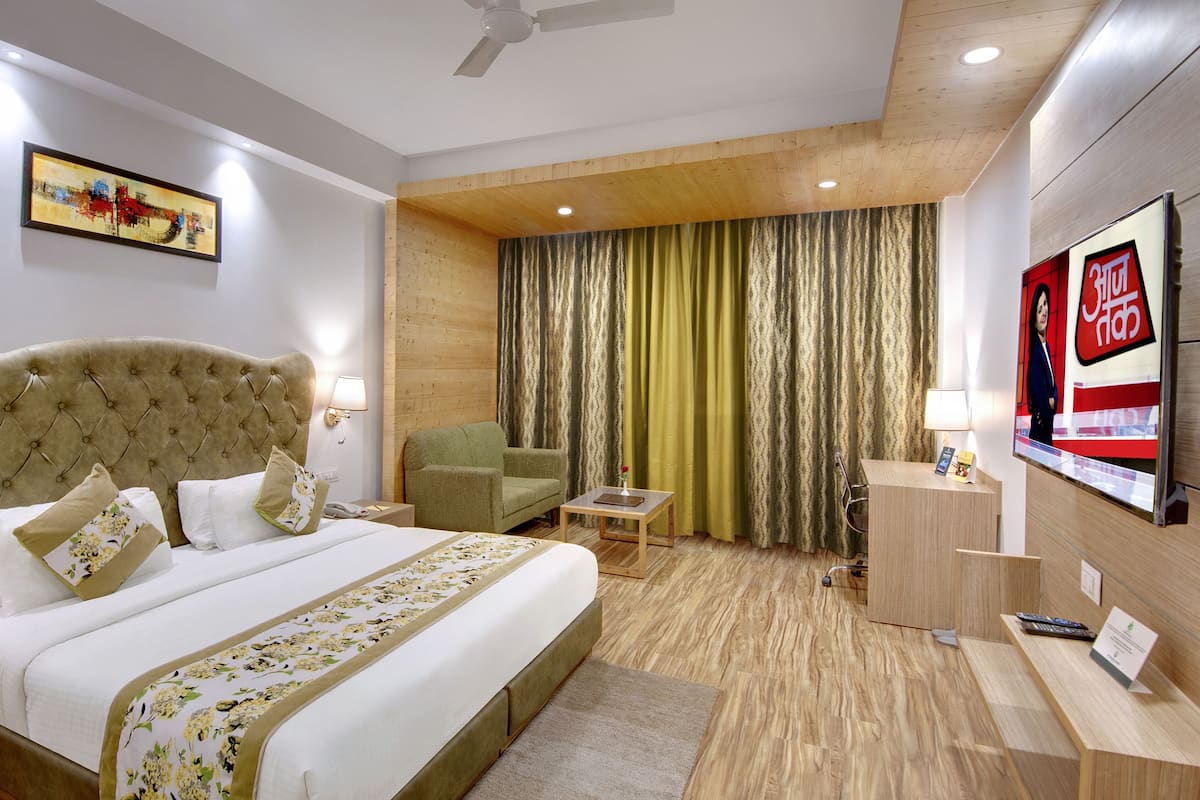 Una habitación de hotel con una cama grande, un sillón verde, un escritorio con computadora y un televisor en la pared.