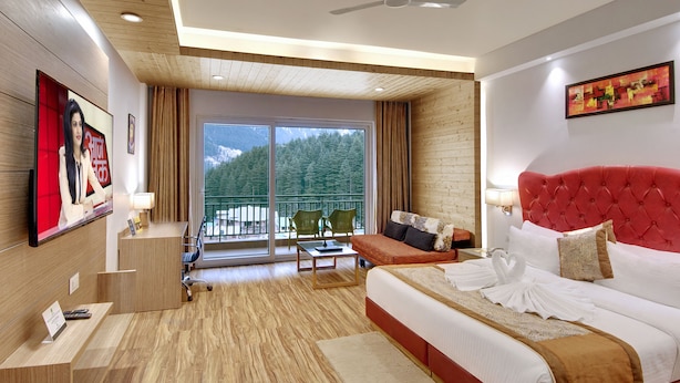 Une chambre d’hôtel avec un grand lit, une tête de lit rouge, un balcon donnant sur la verdure et un bureau avec une chaise.