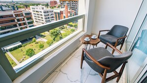 A balcony with two chairs and a small table, overlooking a cityscape with modern buildings and greenery. - Capella Otel (Eskisehir)