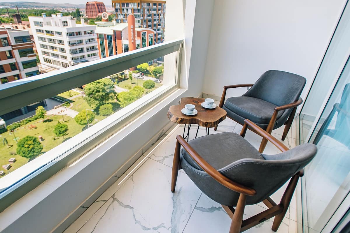 A balcony with two chairs and a small table, overlooking a cityscape with modern buildings and greenery.