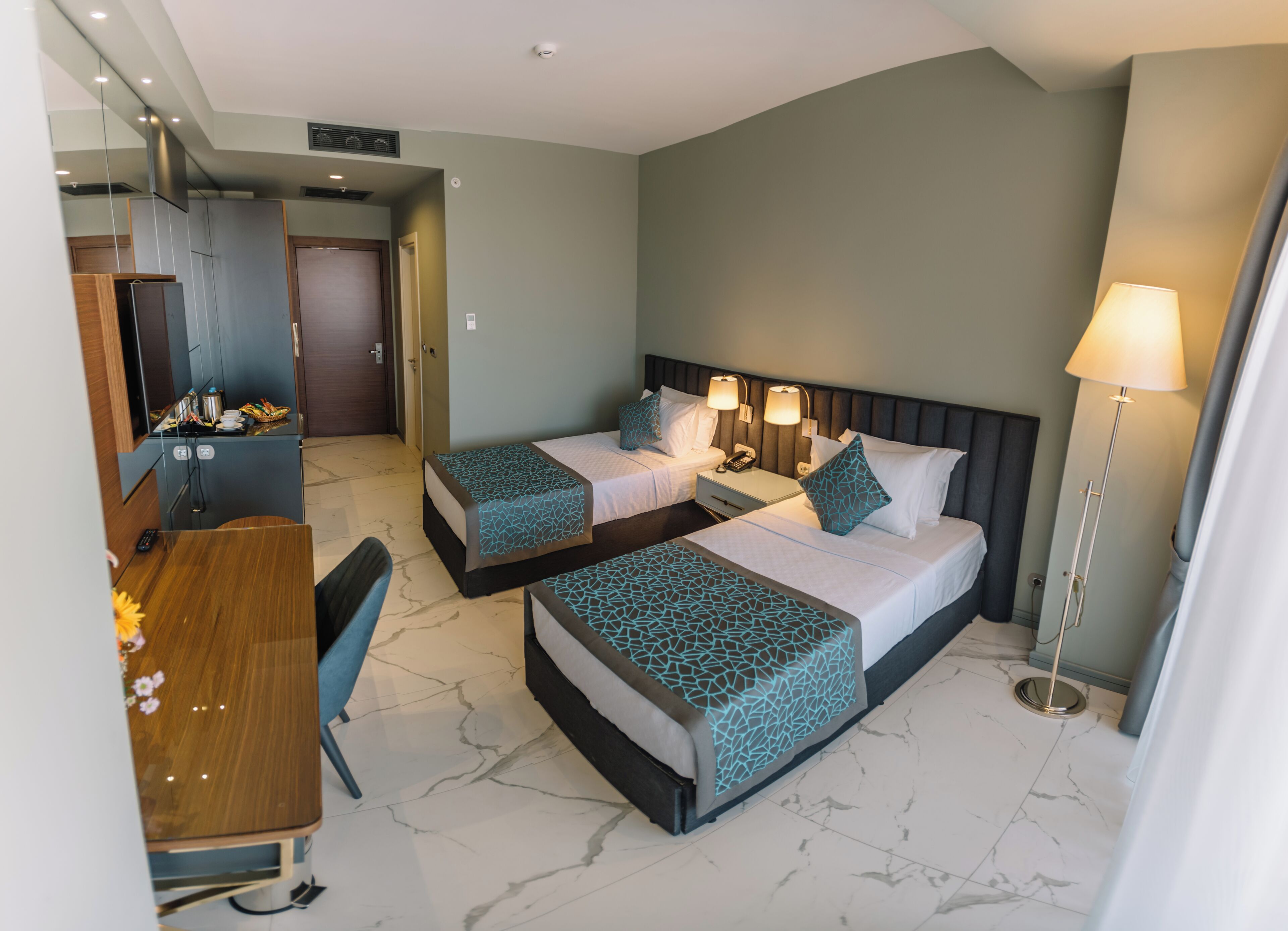 A hotel room with two beds, a desk, a chair, a lamp, and a mirror.
