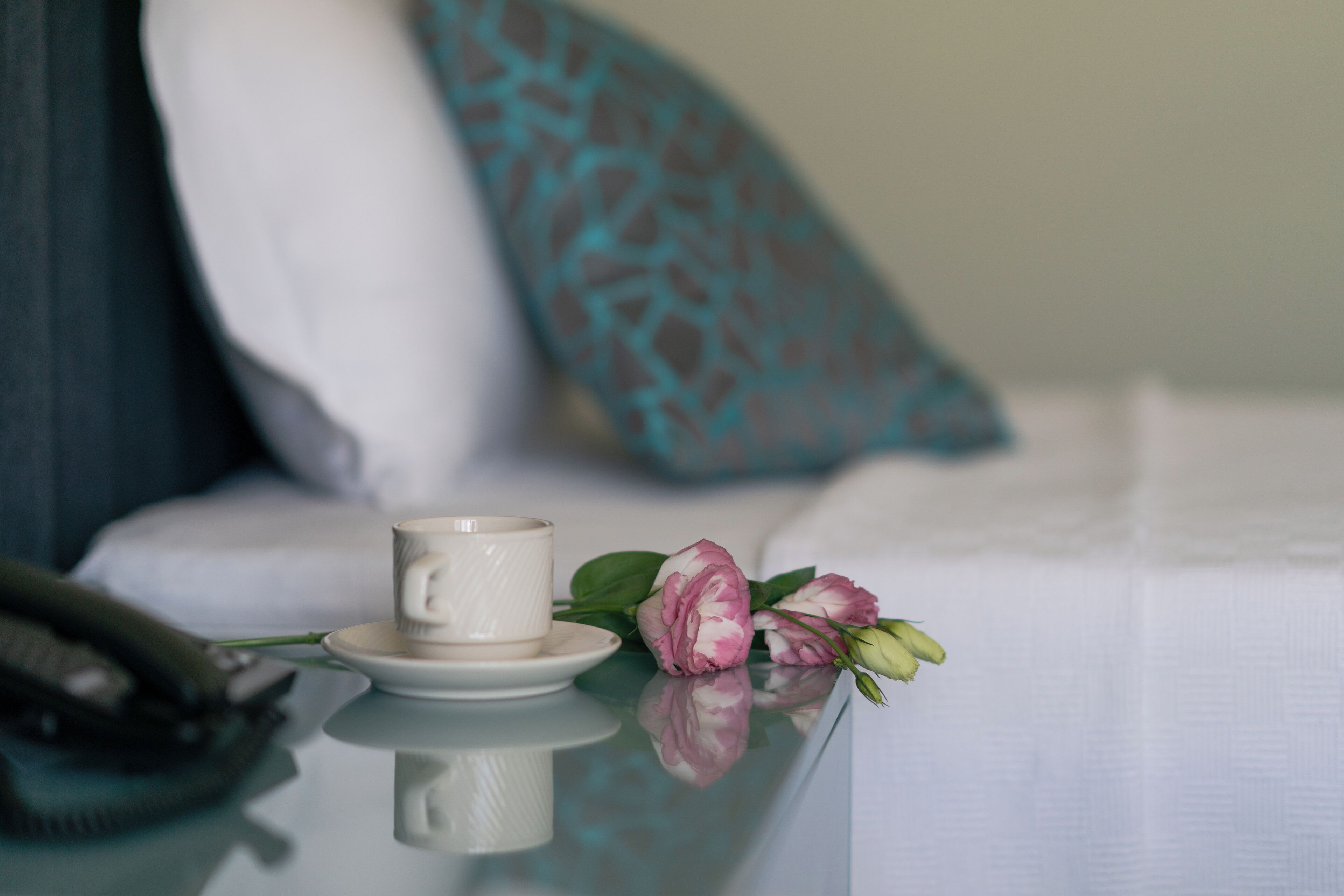 Ein ordentlich gedeckter Tisch mit einer weißen Tasse und Untertasse, einer rosa-weißen Blüte und einem Smartphone.