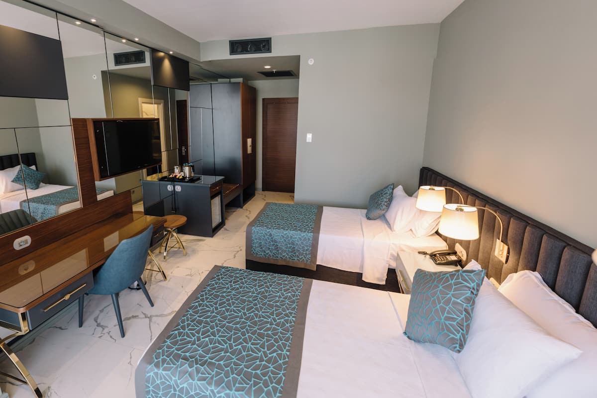 A hotel room with two beds, a desk, a chair, a TV, and a minibar.