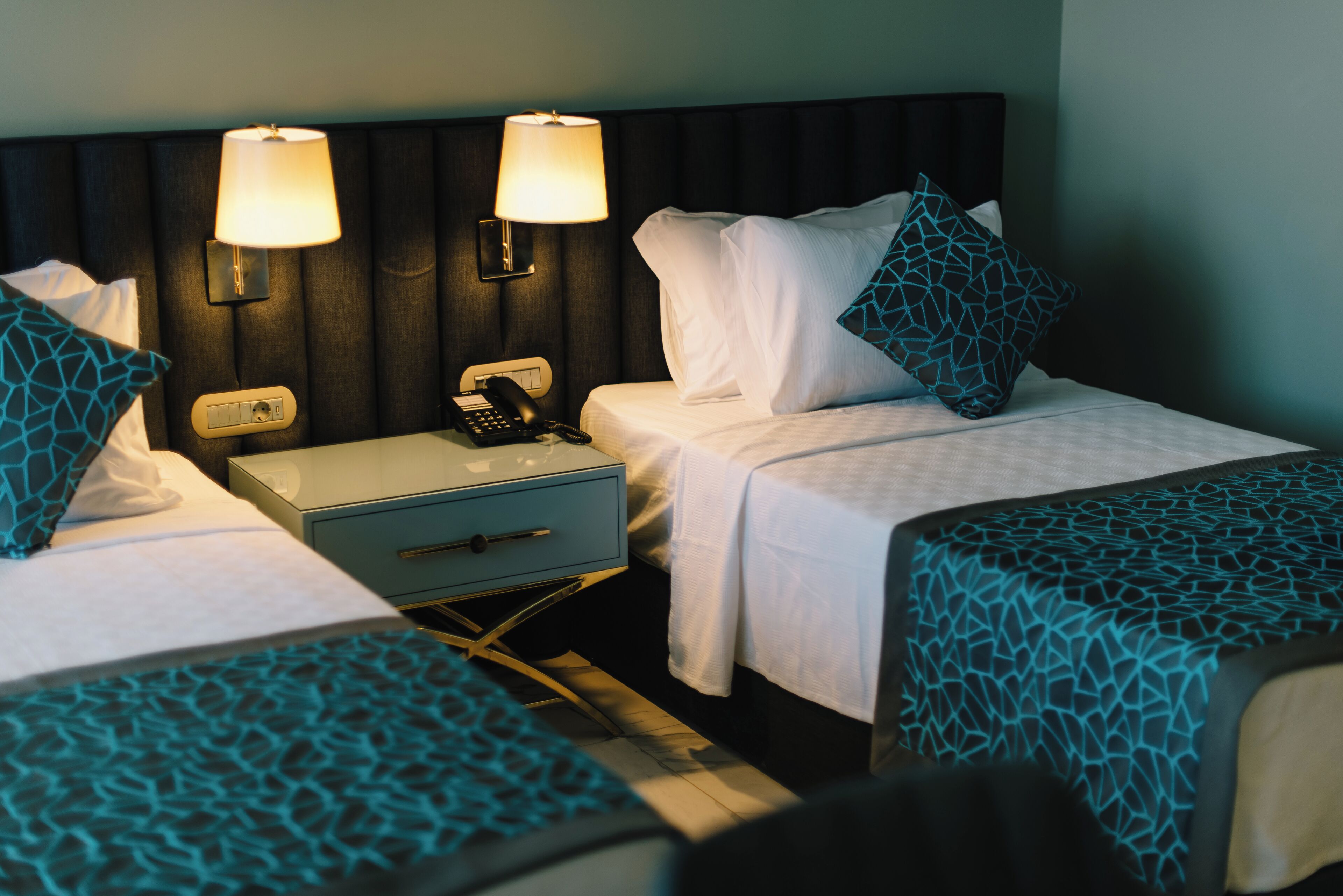 Habitación de hotel con dos camas individuales, una mesita de noche con lámpara, teléfono y cajón.