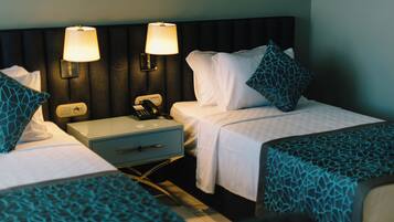 Habitación de hotel con dos camas individuales, una mesita de noche con lámpara, teléfono y cajón.