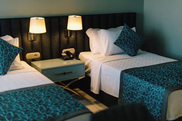 A hotel room with two single beds, a nightstand with a lamp, a phone, and a drawer.