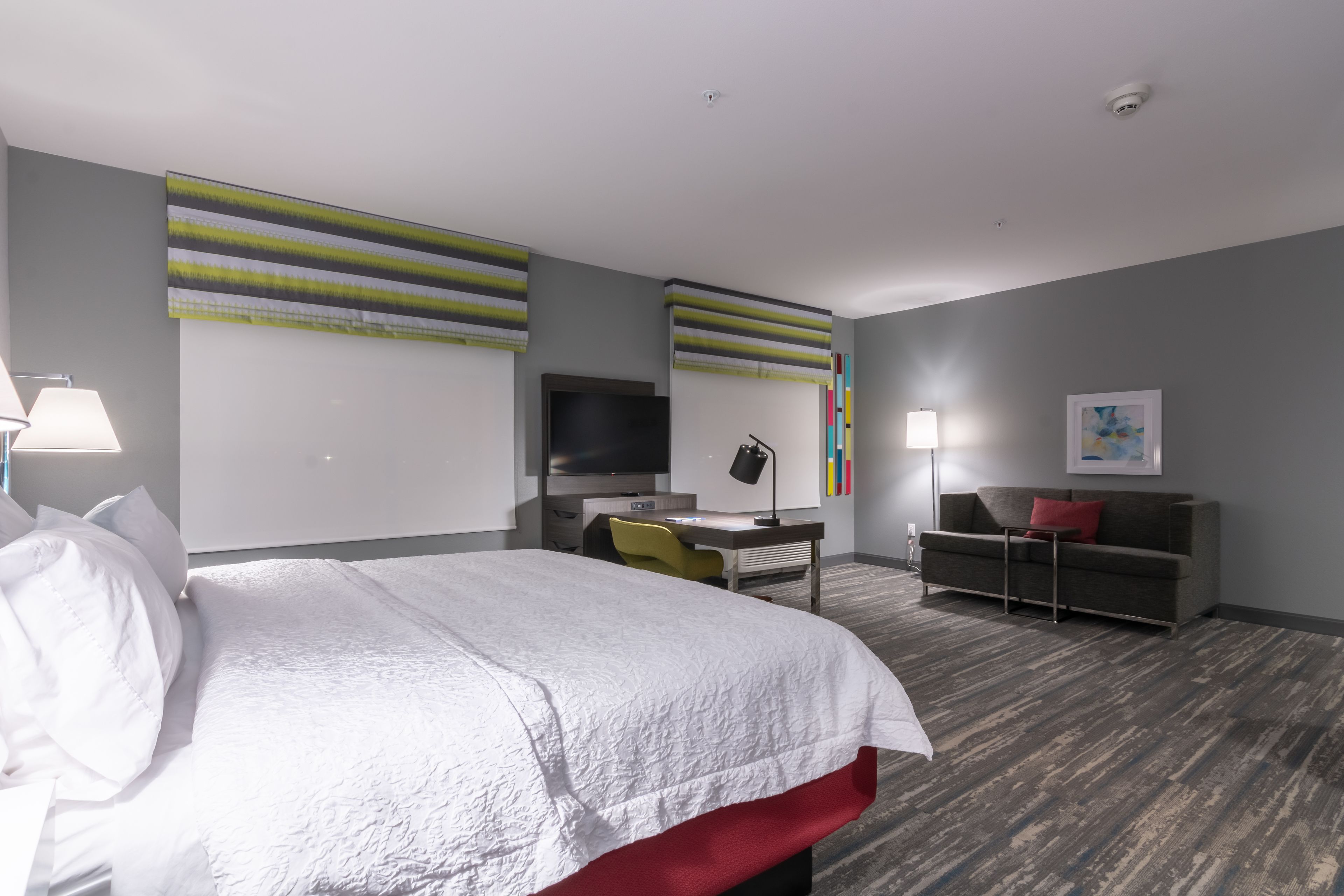 A modern hotel room with a large bed, a desk, a TV, and a sofa.
