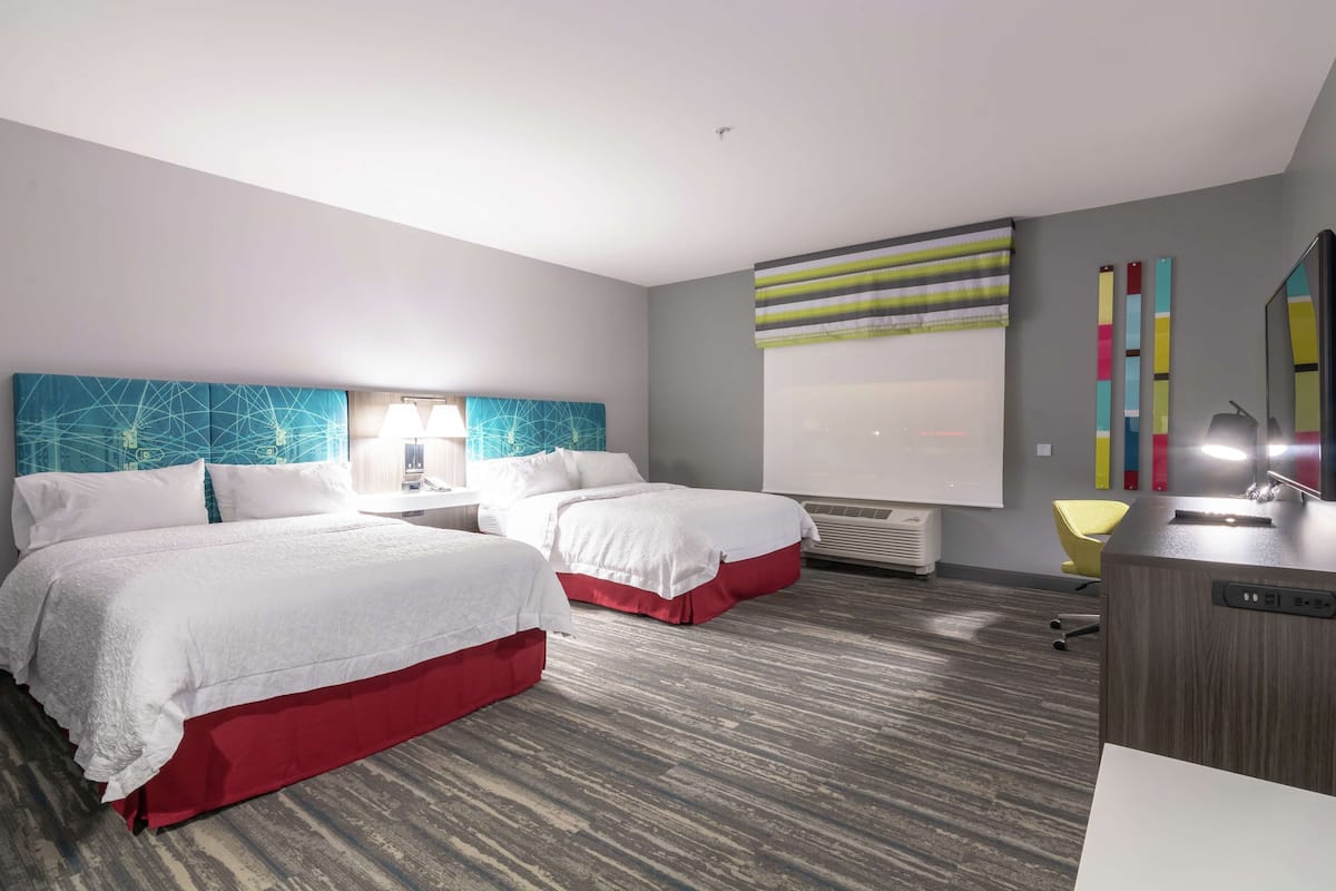 A hotel room with two beds, a desk, a chair, and a large window with a view.