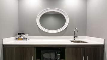 A modern bathroom with a white sink, a round mirror, a built-in microwave, and dark wood cabinets.