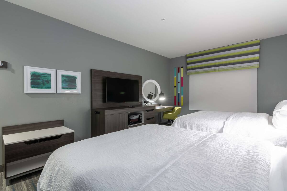 A hotel room with a bed, a desk, a TV, and a mirror.