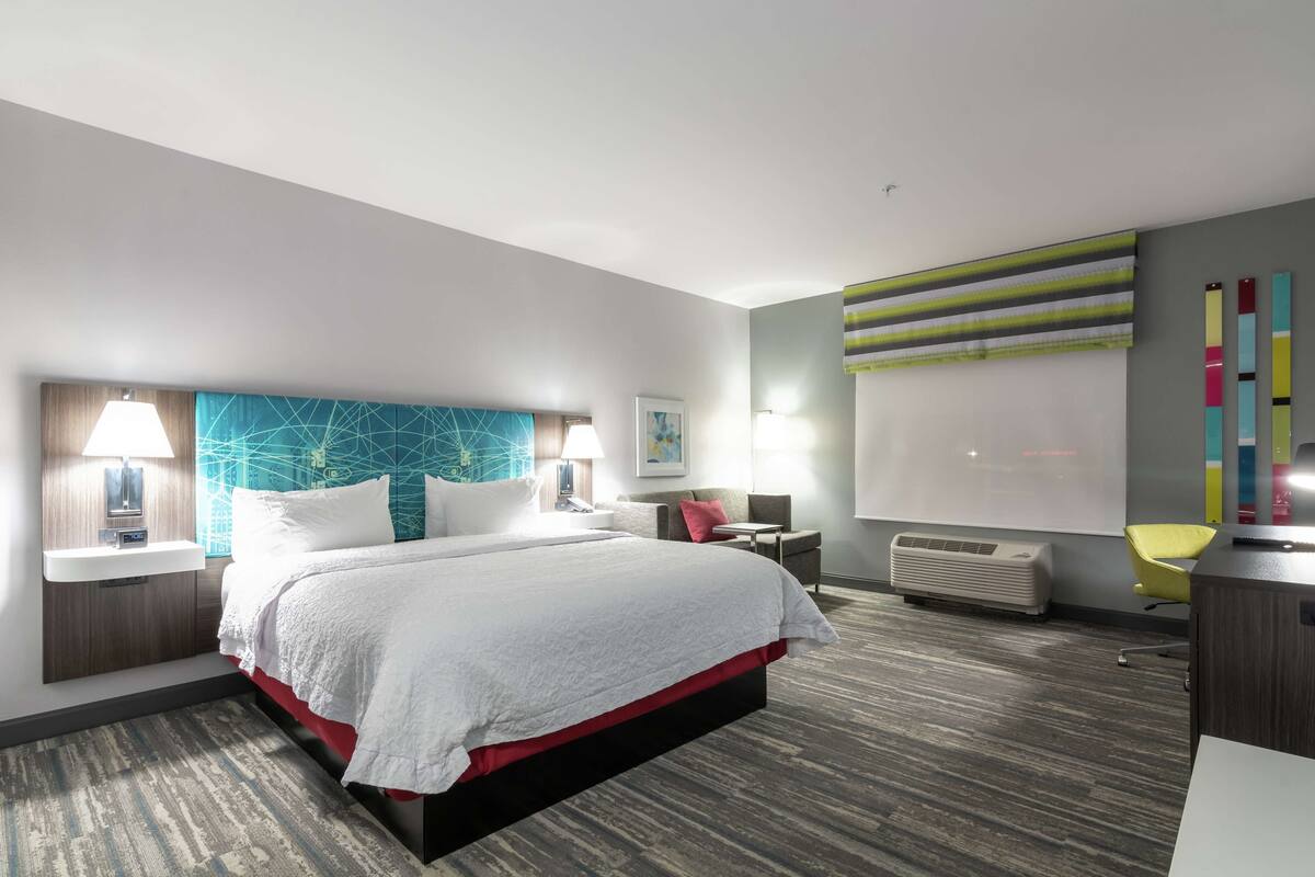 A modern hotel room with a large bed, bedside lamps, a desk, and a chair.