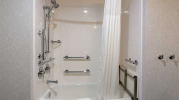 A modern bathroom with a bathtub, shower, and handrails.
