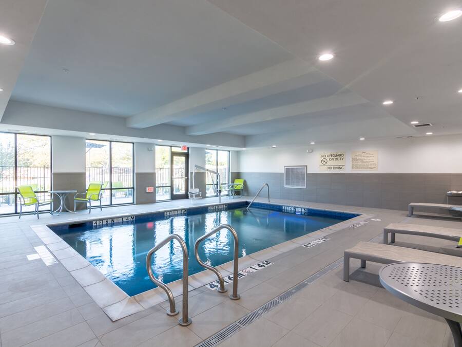 An indoor swimming pool with clear water, metal pool ladders, and yellow chairs around the pool area.