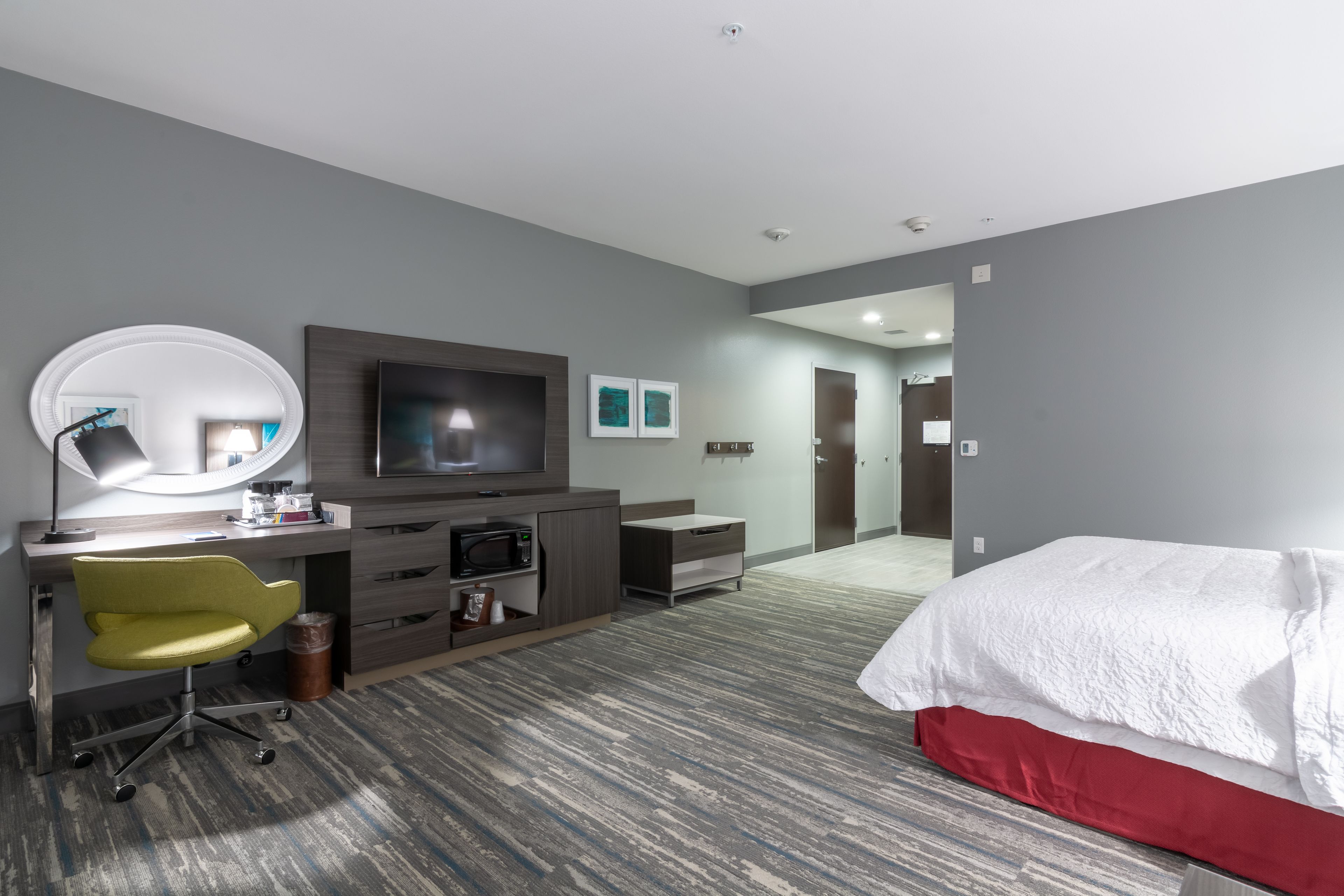 A hotel room with a bed, a desk with a chair, a television, a mirror, and a microwave.